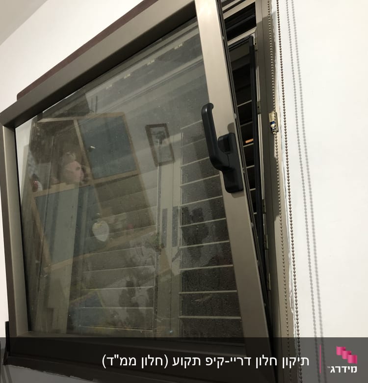 חלון עם תריסים פתוחים וידית שחורה